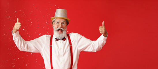 Fototapeta na wymiar Happy Santa Claus showing thumb-up and falling confetti on red background with space for text