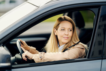 A stylish woman is looking trough the window while driving car on a road.