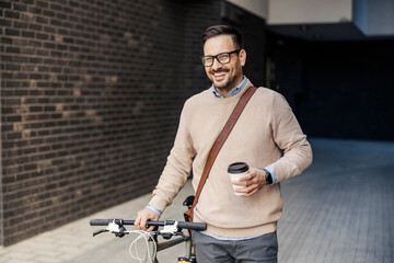 An urban businessman is pushing his bicycle on the street and enjoying takeaway coffee.