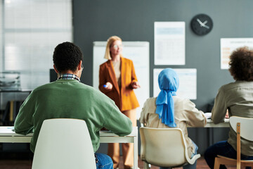 Rear view of multicultural audience listening to teacher and making notes while attending lesson of foreign language in linguistic school