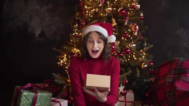 A young beautiful woman is opening a gift box, light shines on her face. 