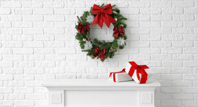 Beautiful Christmas wreath hanging on wall near fireplace with gift boxes on room