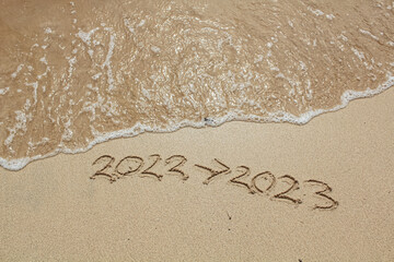 The Sand writing 2022 replaced with 2023 at the beach. New Year's Eve. Merry Chrismast and Happy New Year. 2022 Arrow 2023. Concept for new year greeting cards and calendars. Years sand writing.
