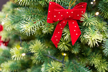 Fototapeta na wymiar Decorated Christmas Tree, Red Bow, Shiny Garland on Green Branches, Blurred Background