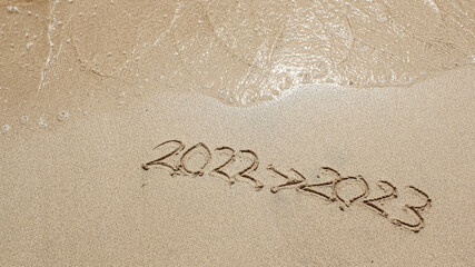 The Sand writing 2022 replaced with 2023 at the beach. New Year's Eve. Merry Chrismast and Happy New Year. 2022 Arrow 2023. Concept for new year greeting cards and calendars. Years sand writing.