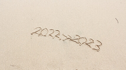 The Sand writing 2022 replaced with 2023 at the beach. New Year's Eve. Merry Chrismast and Happy New Year. 2022 Arrow 2023. Concept for new year greeting cards and calendars. Years sand writing.