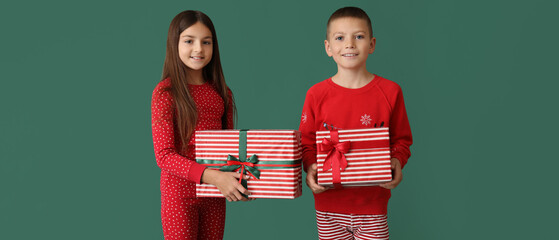 Cute children in Christmas pajamas holding gifts on green background