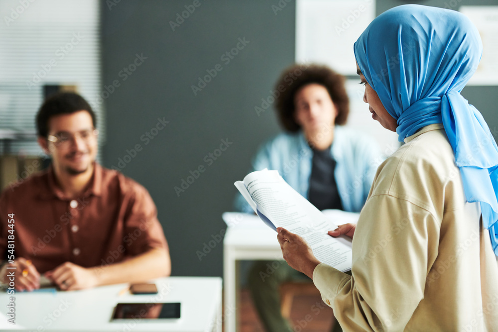 Poster young muslim teacher in blue hijab looking at text in document while making report or explaining new