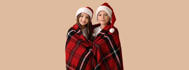 Cute children in pajamas and Santa hats wrapped in plaid on beige background