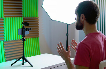 A young blogger records a video with himself on his smartphone in his room studio