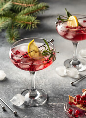 Two wineglass of Pomegranate Christmas cocktail with rosemary and lemon on gray background with fir branches. Xmas drink