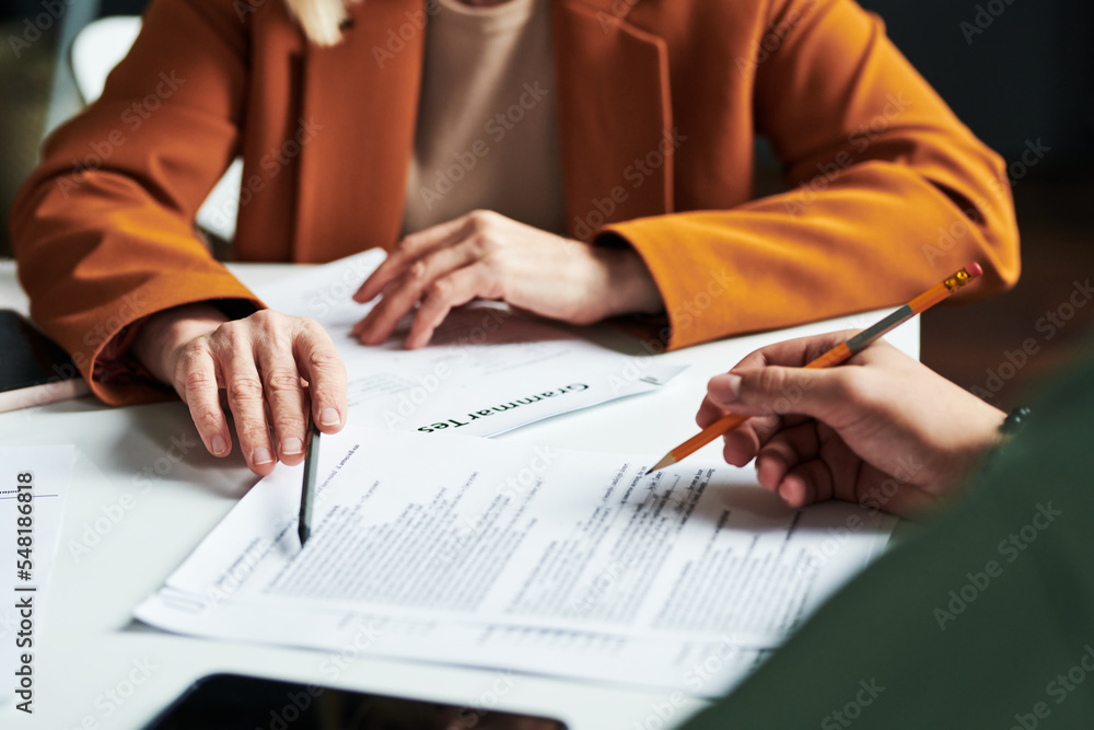 Poster Hand of mature teacher of foreign languages pointing at one of documents while explaining information to student