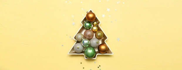 Plate in shape of Christmas tree with balls and confetti on yellow background