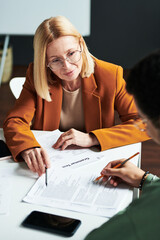 Confident blond mature female teacher of linguistics teaching young man while pointing at one of...