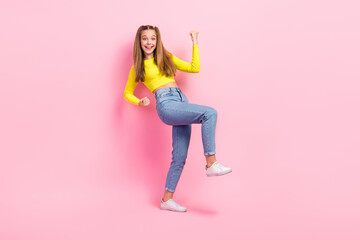 Full length photo of lucky excited school girl dressed yellow crop top walking rising fists isolated pink color background