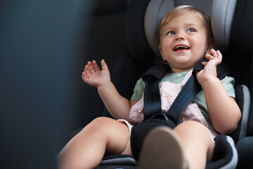 Cute little girl sitting in child safety seat inside car