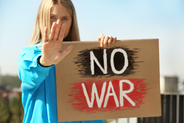 Sad woman holding poster with words No War and showing stop gesture outdoors
