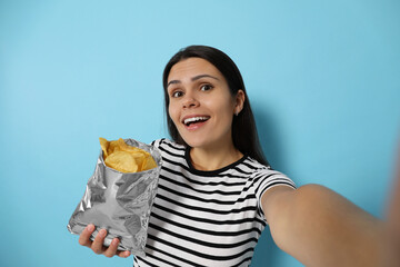 Woman taking selfie with potato chips on light blue background