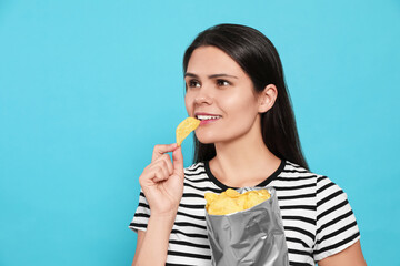 Beautiful woman eating potato chips on light blue background. Space for text