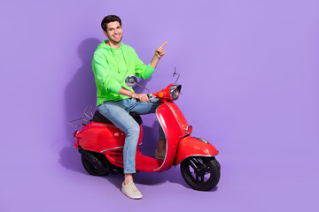 Fototapeta na wymiar Full length photo of satisfied cool guy with brunet hairdo dressed green hoodie directing empty space isolated on purple color background