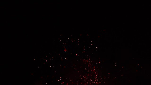 Fire flames with flying sparks on a black background. Firestorm texture. Bokeh lights on black background, shot of flying fire sparks in the air. Sparks from bonfire over dark night background. Slowmo