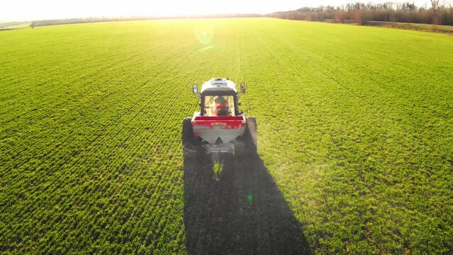 Drone footage tractor spreading artificial fertilizers in green field. Farming tractor spraying on field with herbicides. Industrial machine fertilizing a field.Chemicals used by agricultural tractor.