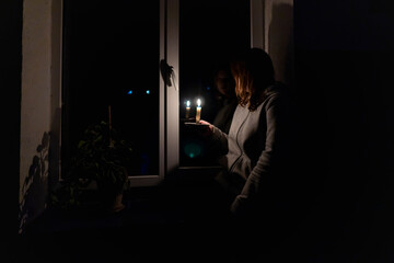 Blackout. Girl with a burning candle in a dark room sits near the window