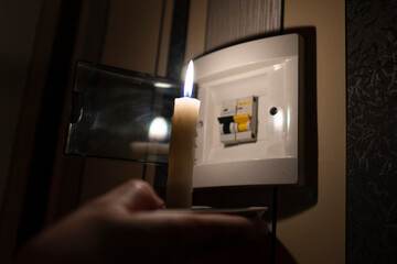 Blackout. A hand with a burning candle illuminates an electrical switchboard