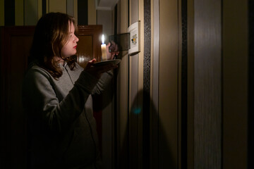 Blackout. A girl with a burning candle checks the electrical switchboard in the room
