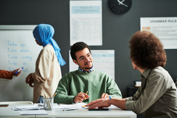 Confident Middle Eastern man looking at classmate and listening to him at lesson against young...