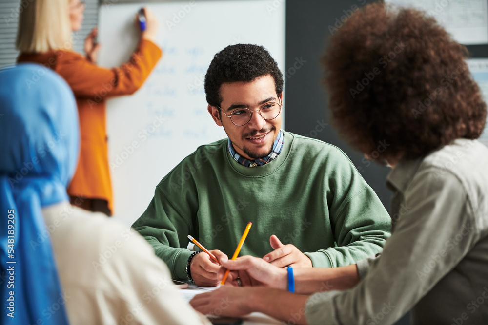 Poster happy young man in eyeglasses communicating with another student at break between lessons against te