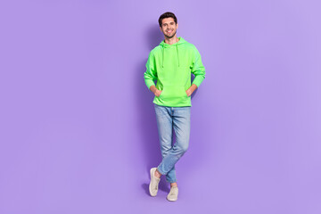 Fototapeta premium Full body size photo of attractive guy wear bright green hoodie stylish jeans confident empty space new brand isolated on purple color background