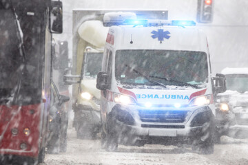 911 ambulance van rushing through traffic during heavy winter snowfall conditions. © astrosystem