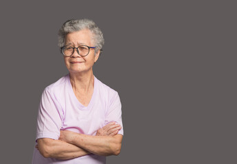 Beautiful elderly Asian woman looking at the camera with a smile while standing on a gray background