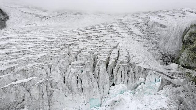 Aerial flyover over the edge of the Moiry glacier near Grimentz in Valais, Switzerland with a spinning view of the icy crevasses, valley and lake on a cloudy summer afternoon