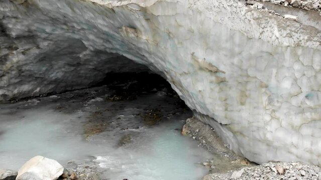 Aerial flyover from the ice cave of the Zinal glacier in Valais, Switzerland with a view of the melting glacial water stream and crevasses