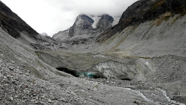 Aerial flyover towards the end of the Zinal glacier in Valais, Switzerland with a view of the melting glacial water stream and the alpine valley
