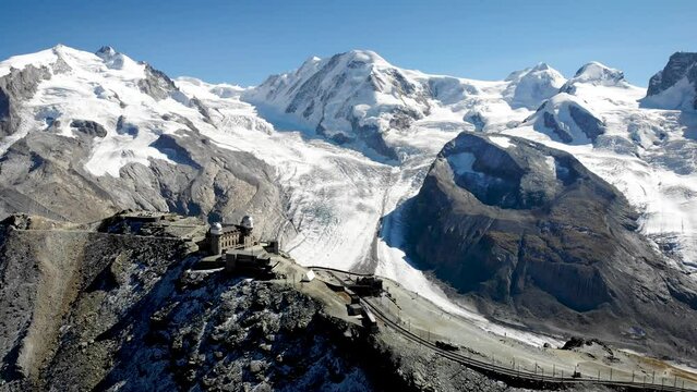 Aerial flyover over Gornergrat in Zermatt, Switzerland with view of the train station and of the famous observatory along with Monte Rosa, Dufourspitze and Gorner glacier in the background