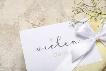 Card with text VIELEN DANK, gift box and flowers on grunge background