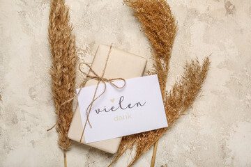 Card with text VIELEN DANK, gift box and pampas grass on grunge background