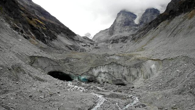 Aerial flyover into the ice cave of the Zinal glacier in Valais, Switzerland with a view of the melting glacial water stream in alpine valley