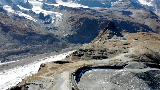 Aerial view of a train leaving  Gornergrat in Zermatt, Switzerland with panning view from the Matterhorn along the train tracks overlooking the glacier and Dufourspitze, Monte Rosa and observatory