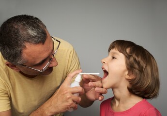 Dad takes care of his daughter treats a sore throat. The girl opened her mouth wide for irrigation