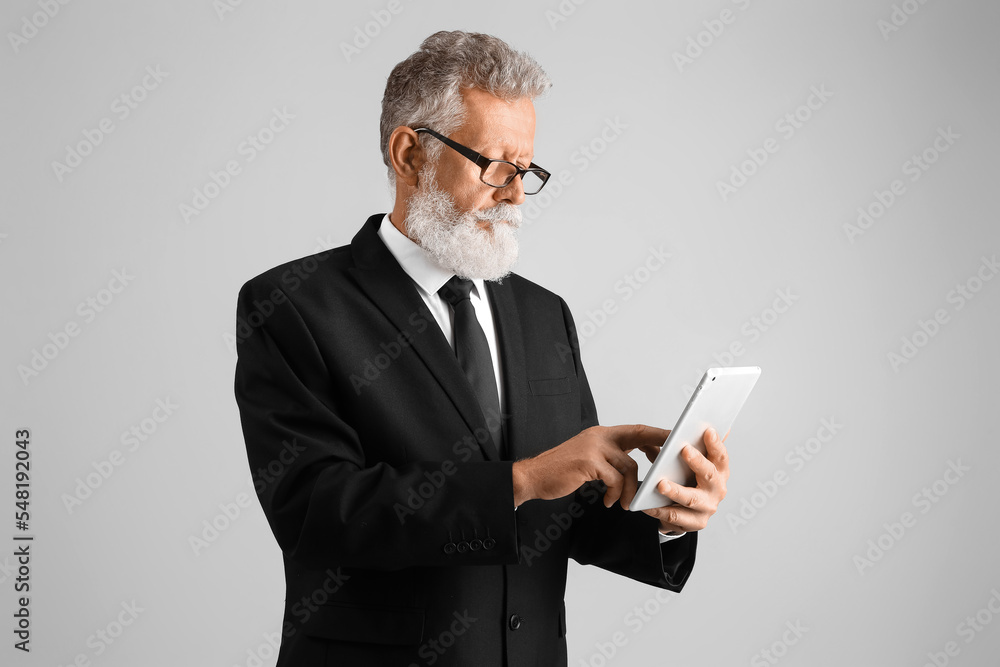 Poster senior man in suit using tablet computer on grey background