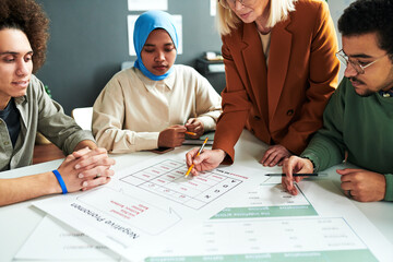 Mature blond teacher bending over document with table of pronouns while explaining new subject to...