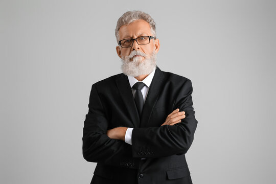 Senior bearded man in eyeglasses and black suit on grey background