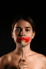 Young woman painting her mouth on dark background. Censorship concept