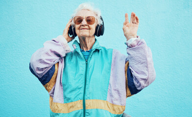 Happy, elderly and woman with headphone music for wellness, fun and retirement leisure. Urban, retro and funky senior person listening to feel good streaming on headphones at blue wall. - obrazy, fototapety, plakaty
