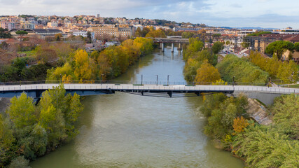 Fototapeta na wymiar Aerial view over the Tiber River and the Ponte della Scienza, a pedestrian bridge that connects the Lungotevere in Rome, Italy, between the Portuense and Ostiense districts.
