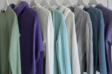 Rack with knitted sweaters near light wall, closeup